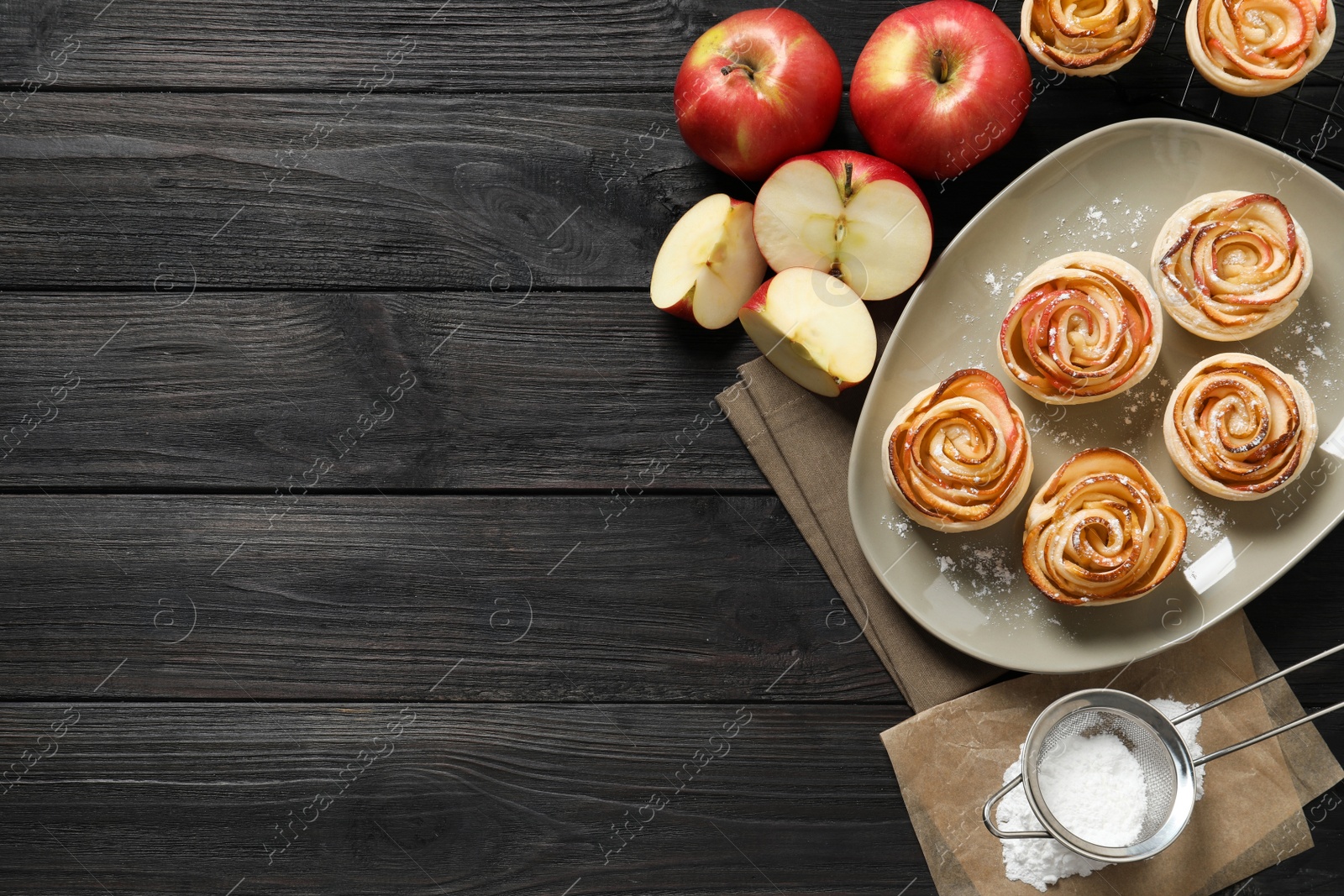 Photo of Freshly baked apple roses on dark wooden table, flat lay. Space for text
