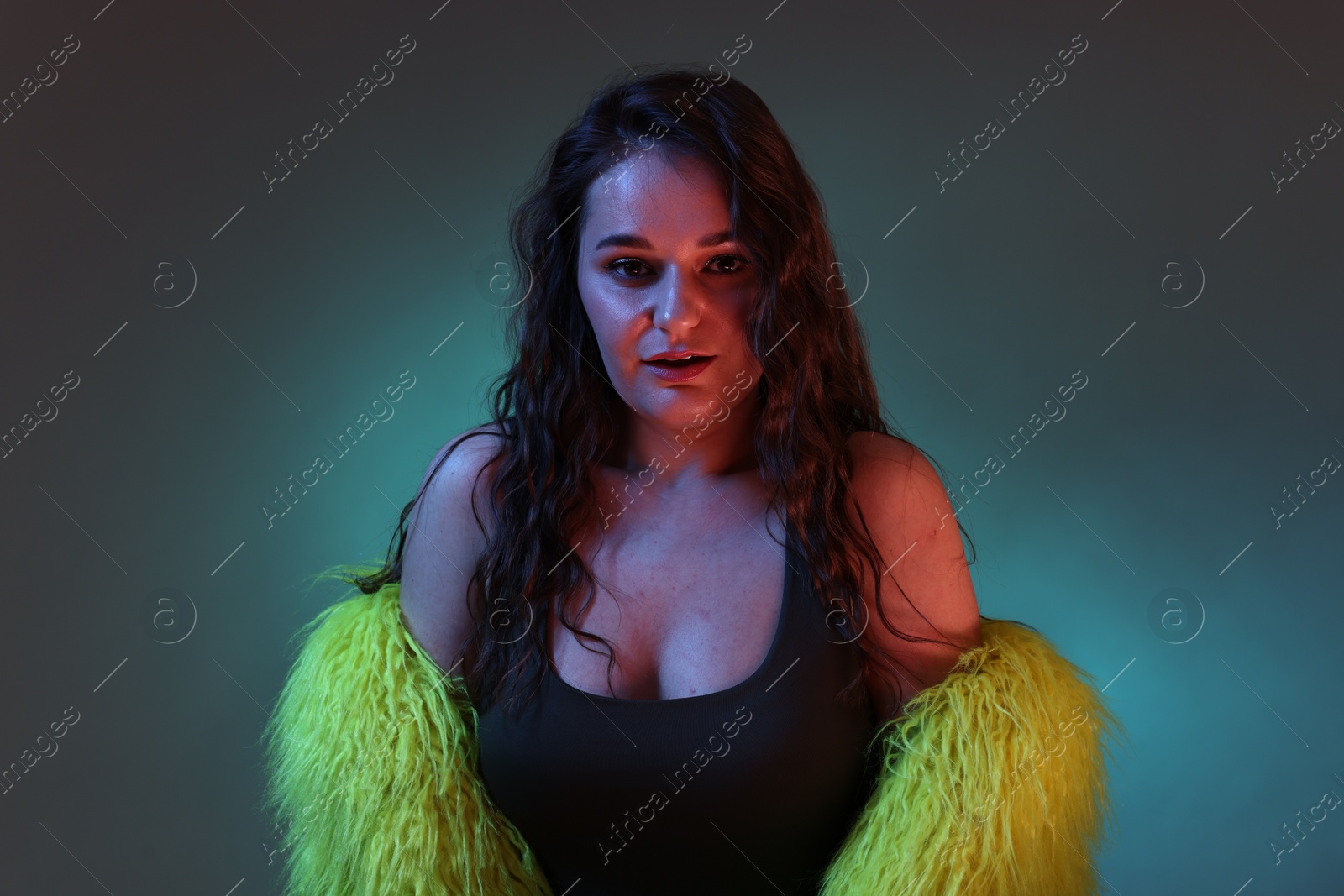 Photo of Portrait of beautiful woman in yellow fur coat on dark background with neon lights