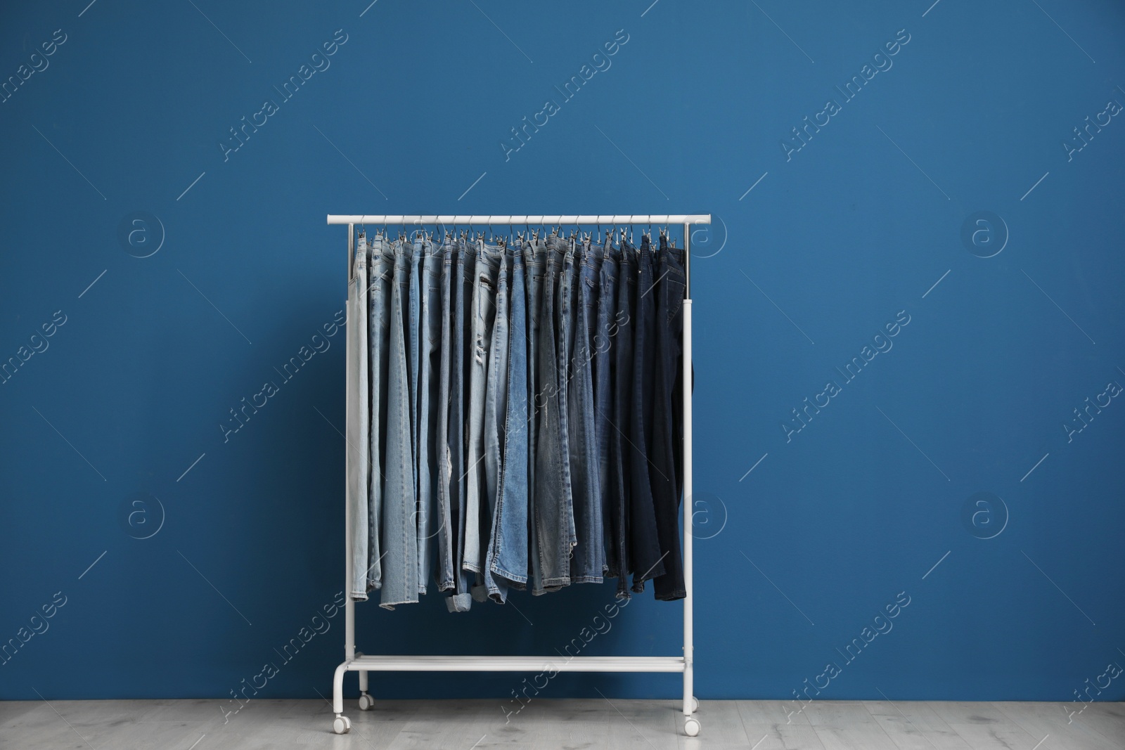 Photo of Rack with stylish jeans near blue wall