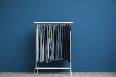 Rack with stylish jeans near blue wall