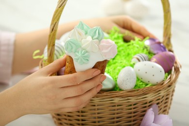 Photo of Closeup of woman holding delicious Easter cake with meringues near wicker basket, closeup