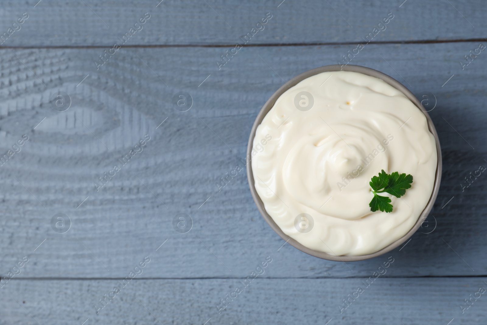 Photo of Tasty mayonnaise and parsley in bowl on gray wooden table, top view. Space for text