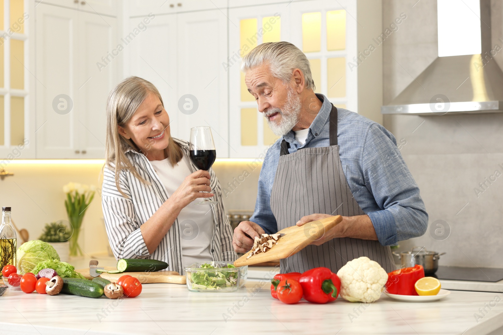 Photo of Happy senior couple cooking together in kitchen. Woman with glass of wine near her husband