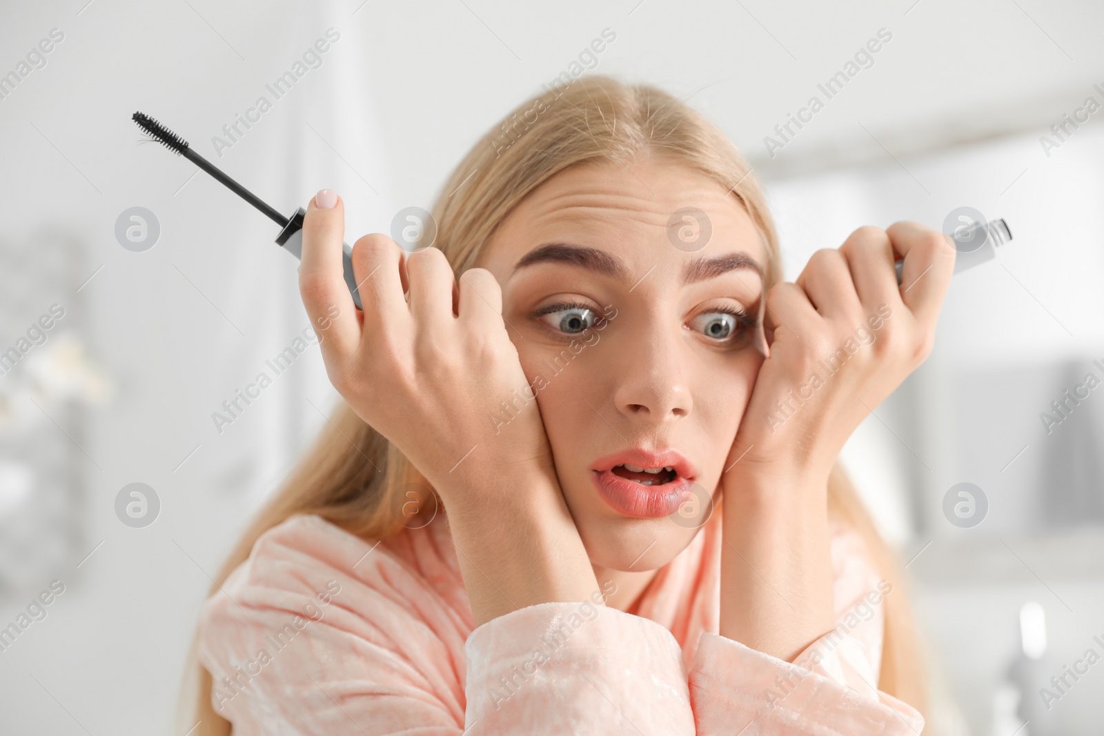 Photo of Emotional woman holding mascara brush with fallen eyelashes indoors