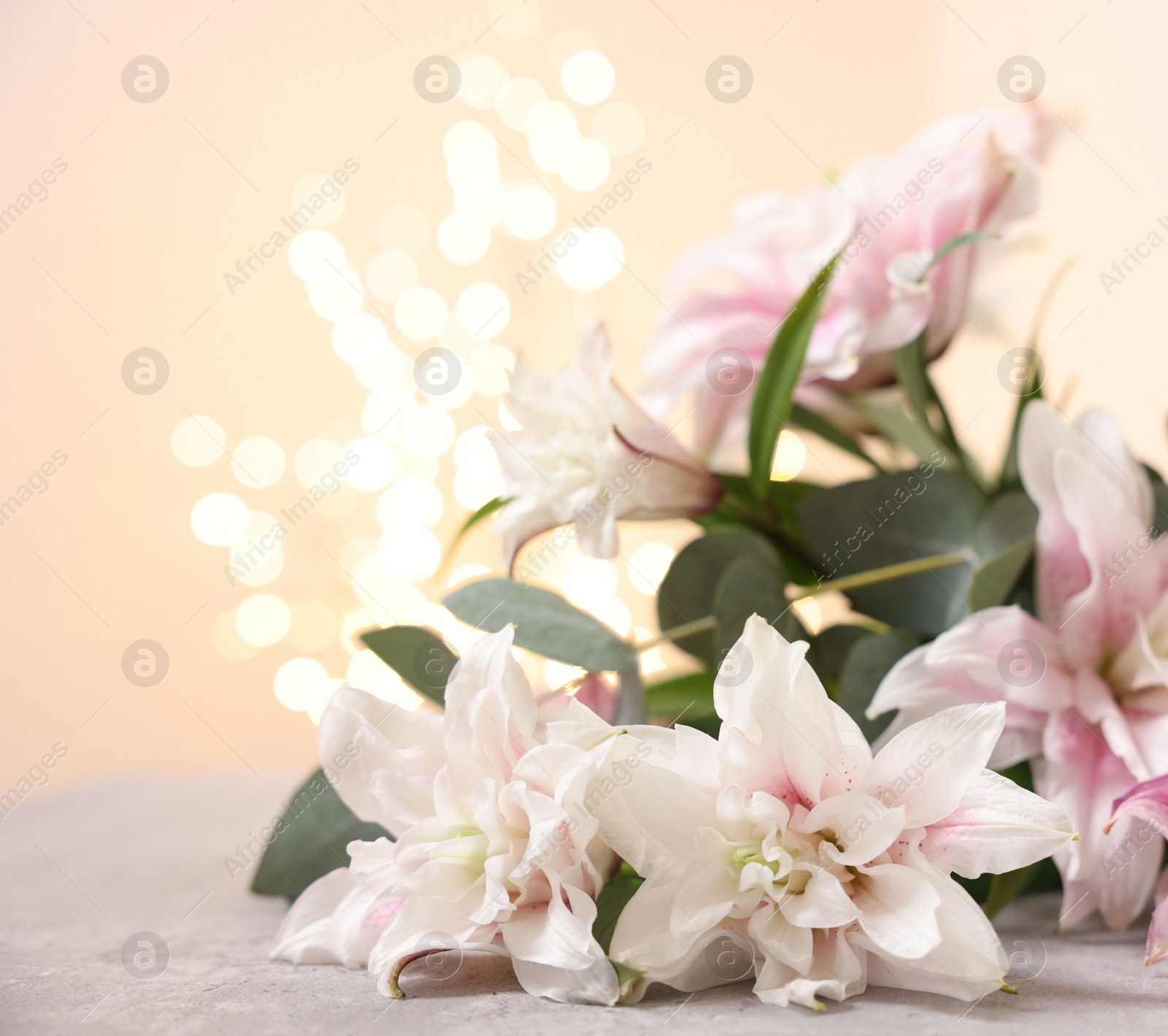 Photo of Bouquet of beautiful lily flowers on table against beige background with blurred lights, closeup