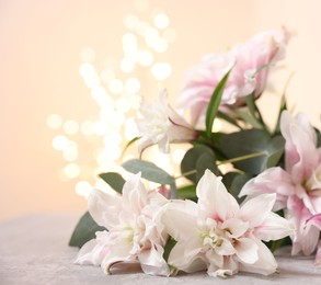 Photo of Bouquet of beautiful lily flowers on table against beige background with blurred lights, closeup