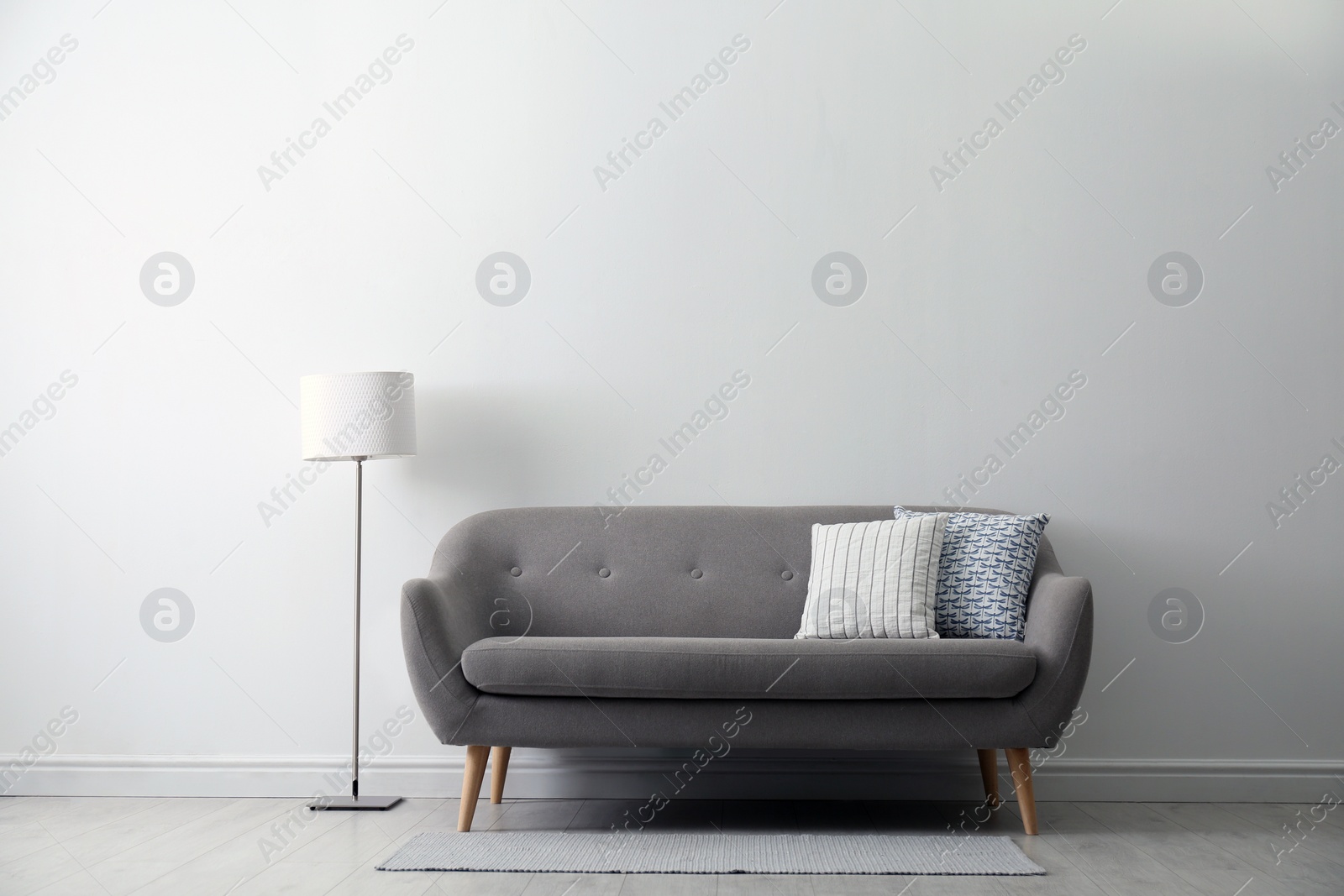 Photo of Grey sofa with pillows near white wall in stylish living room interior