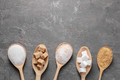 Photo of Spoons with different types of sugar on gray textured table, flat lay. Space for text