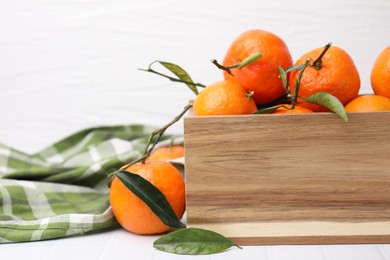 Photo of Wooden crate with fresh ripe tangerines and leaves on white table, closeup. Space for text