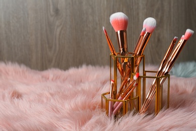 Organizer with set of professional makeup brushes on furry fabric against wooden background. Space for text