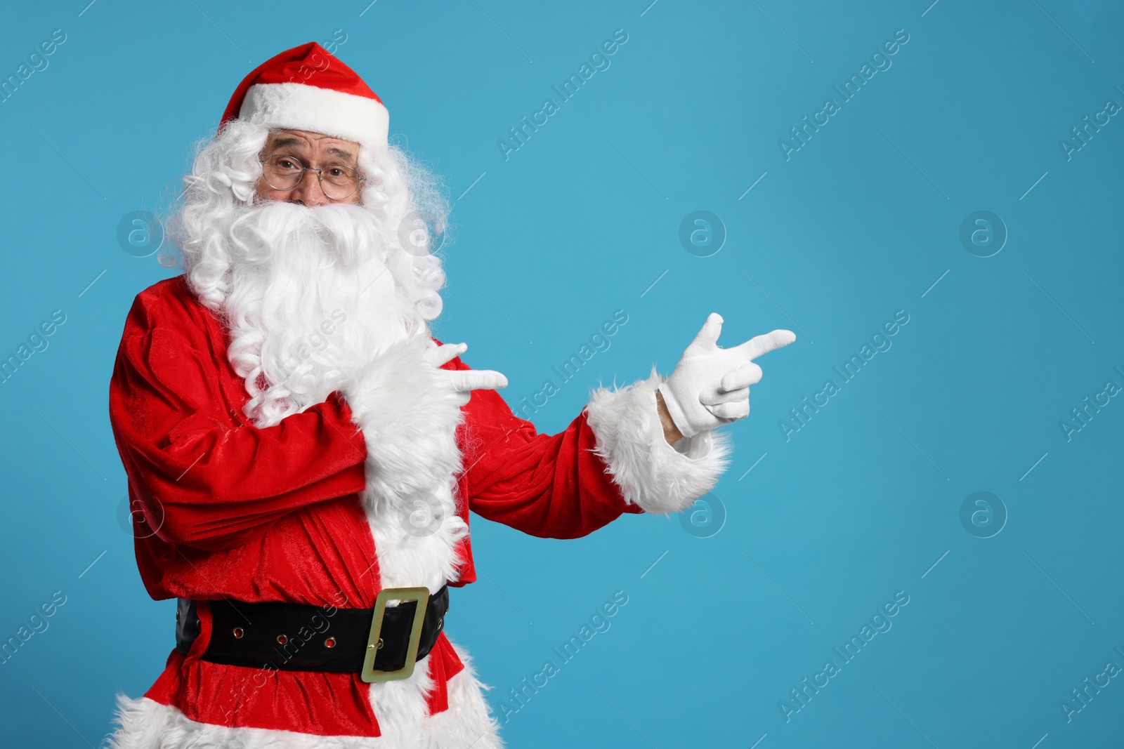 Photo of Merry Christmas. Santa Claus pointing at something on light blue background, space for text