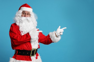 Merry Christmas. Santa Claus pointing at something on light blue background, space for text