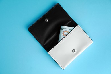 Photo of Open leather purse with money on light blue background, top view