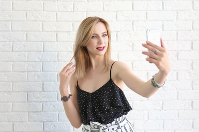 Photo of Attractive young woman taking selfie near brick wall