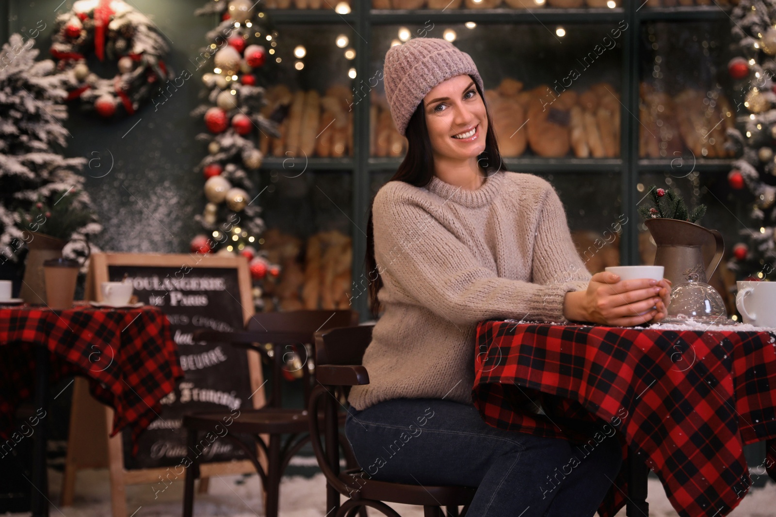 Photo of Beautiful woman at table in decorated cafe. Christmas celebration