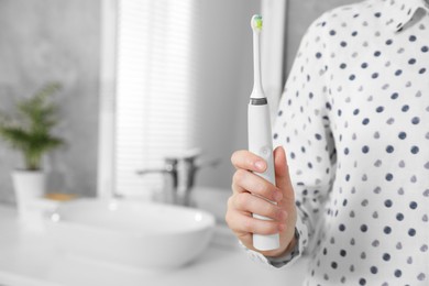 Photo of Woman holding electric toothbrush in bathroom at home, closeup. Space for text