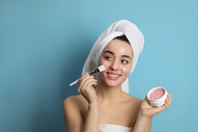 Photo of Woman applying pomegranate face mask on light blue background