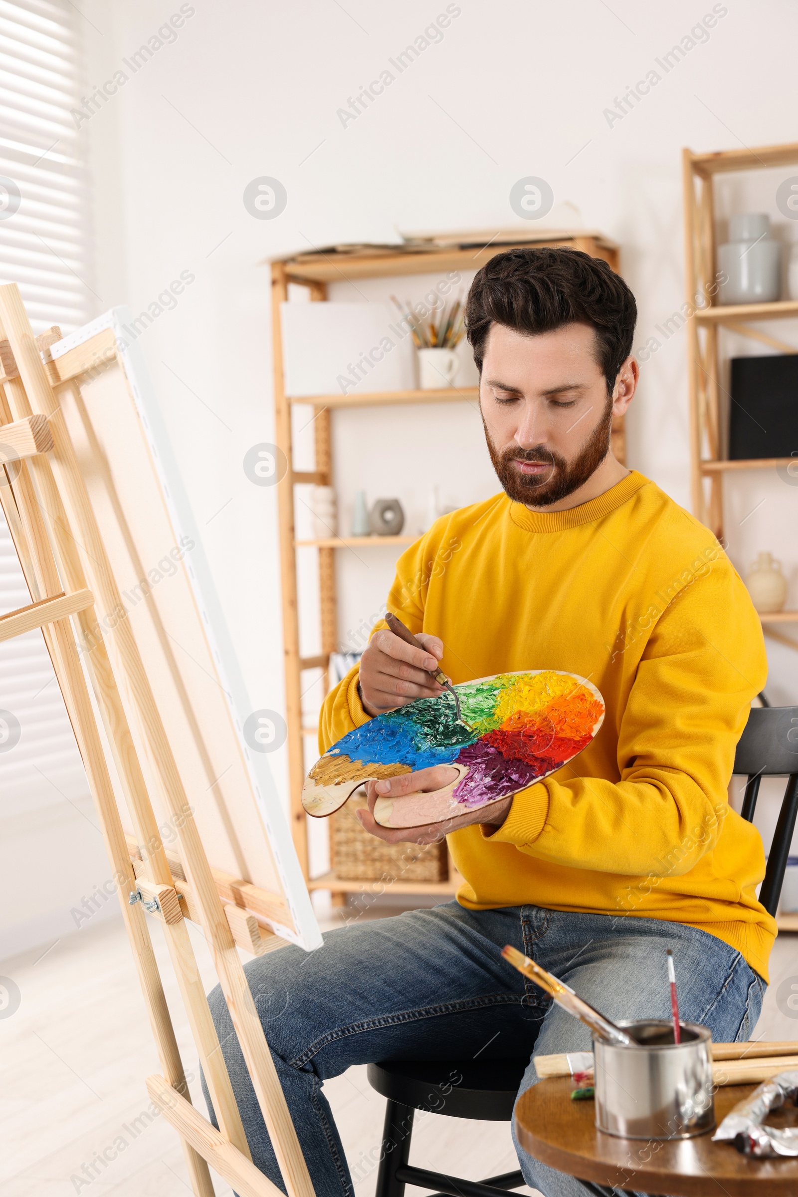 Photo of Man painting in studio. Using easel to hold canvas