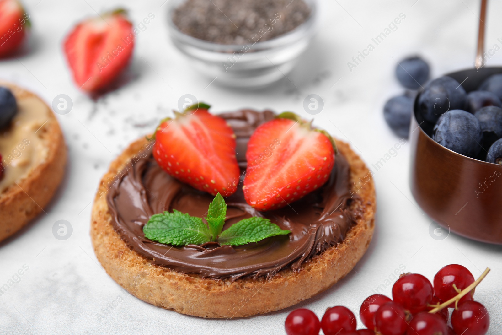 Photo of Tasty organic rusk with chocolate spread, strawberry and mint on white marble table, closeup