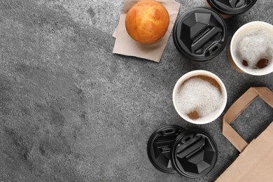 Coffee to go. Paper cups of tasty drink and muffin on grey table, flat lay with space for text