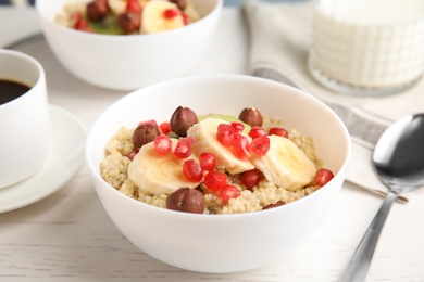 Bowl of quinoa porridge with hazelnuts, kiwi, banana and pomegranate seeds served for breakfast on white wooden table