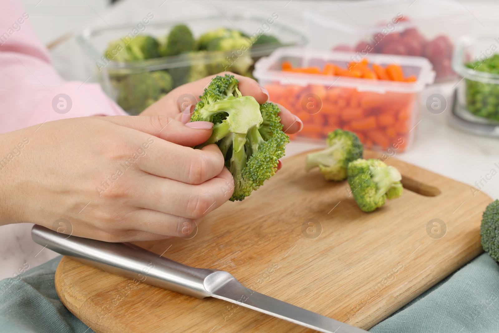 Photo of Woman holding green broccoli near containers with fresh products at table, closeup