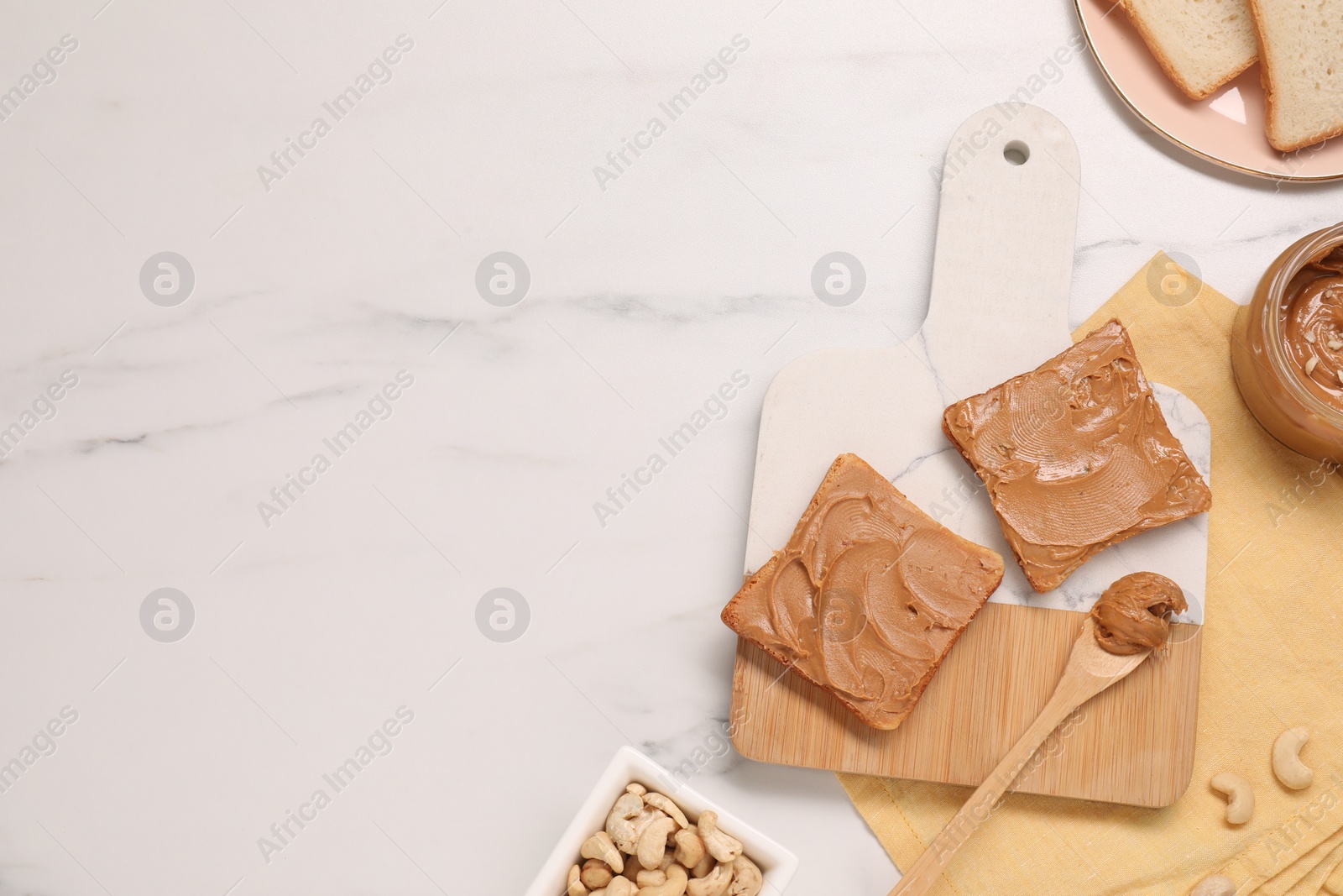 Photo of Toasts with tasty nut butter and cashews on white marble table, flat lay. Space for text