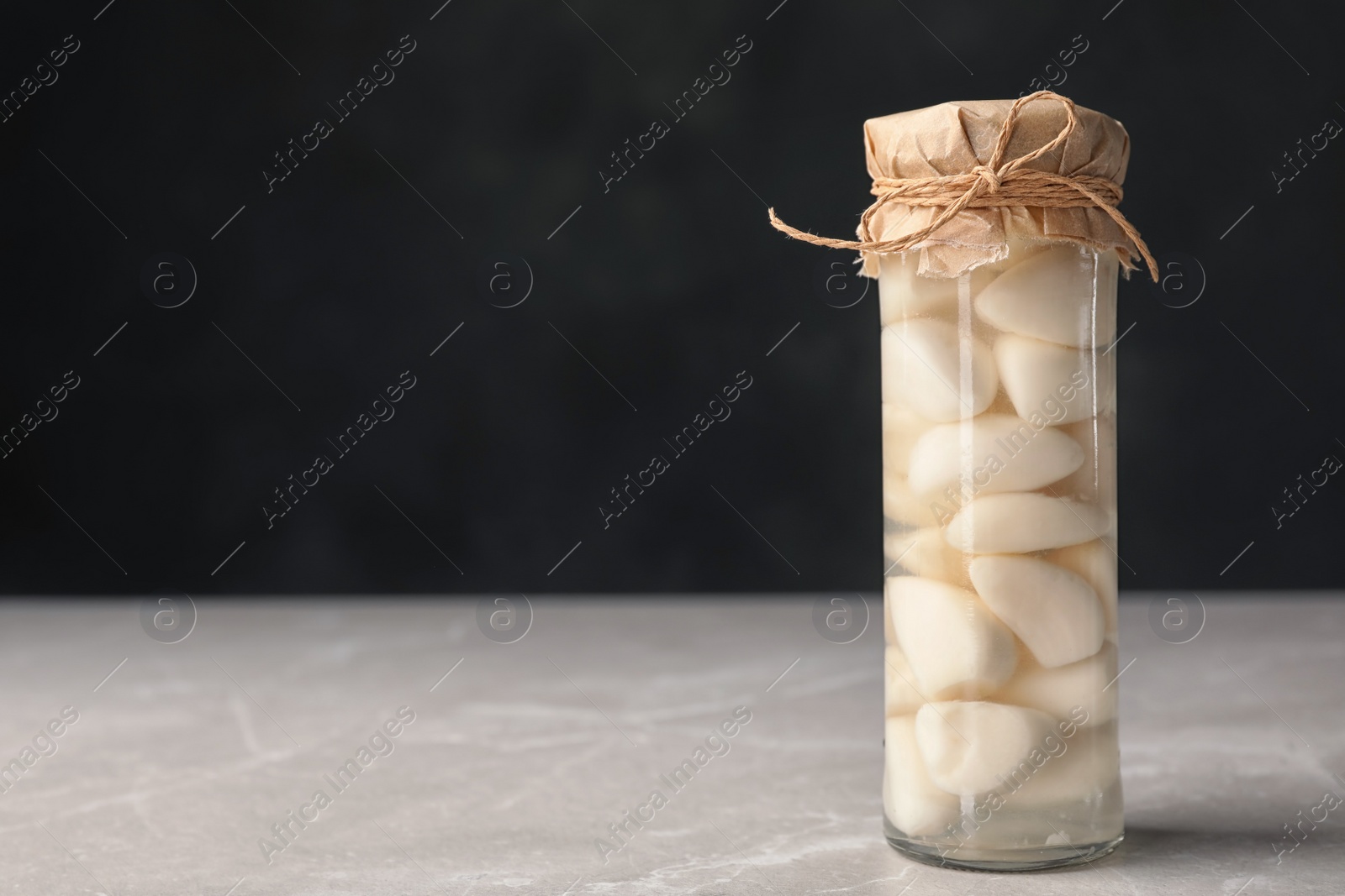 Photo of Preserved garlic in glass jar on table. Space for text