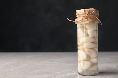 Photo of Preserved garlic in glass jar on table. Space for text