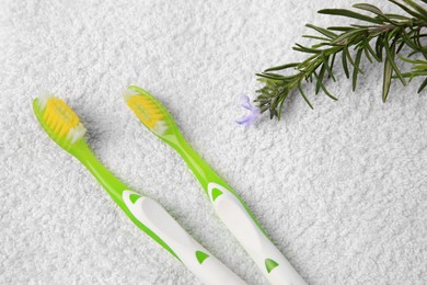 Photo of Light green toothbrushes and rosemary on white terry towel, flat lay