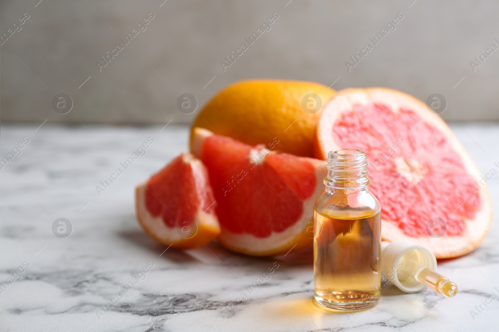 Photo of Bottle of essential oil, pipette and fresh grapefruits on marble table, space for text