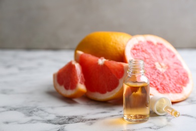 Bottle of essential oil, pipette and fresh grapefruits on marble table, space for text