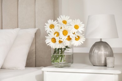 Photo of Bouquet of beautiful daisy flowers and lamp on nightstand in bedroom