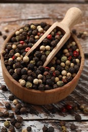 Photo of Aromatic spice. Different peppers in bowl and scoop on wooden table, closeup