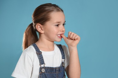 Photo of Cute little girl biting her nails on turquoise background