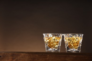 Photo of Whiskey in glasses on wooden table against brown background, space for text