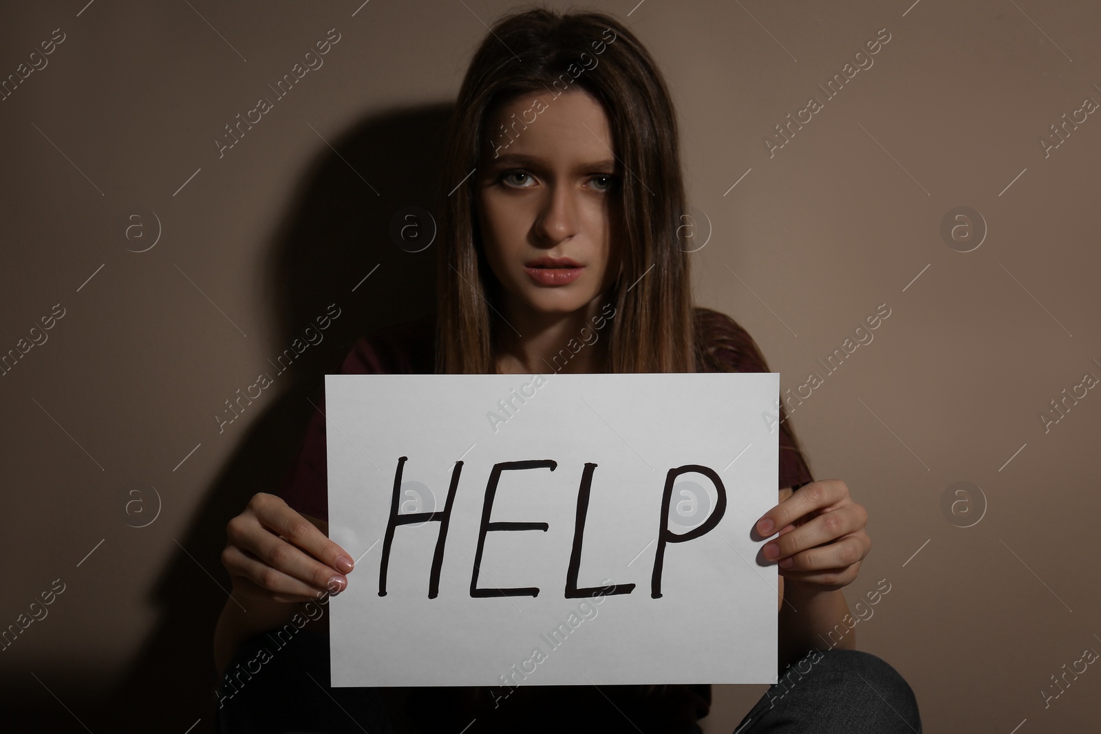 Photo of Abused young woman with sign HELP near beige wall. Domestic violence concept