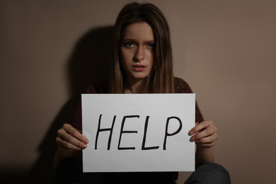 Photo of Abused young woman with sign HELP near beige wall. Domestic violence concept