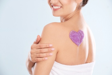Young woman with heart made of body scrub on her back against white background