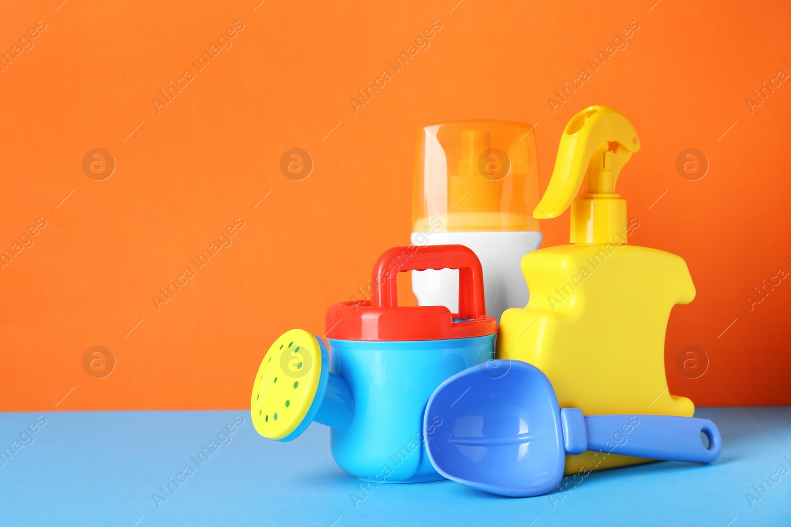 Photo of Different suntan products and plastic beach toys on color background. Space for text