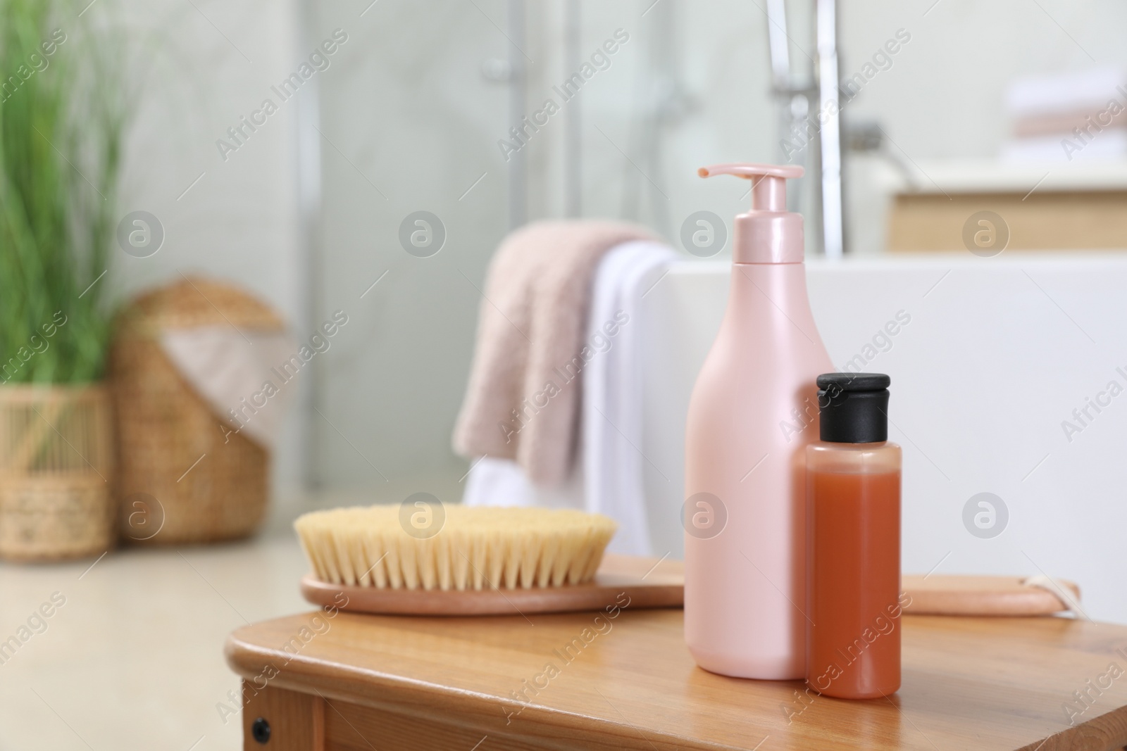 Photo of Bottles of shower gels and brush on wooden table near tub in bathroom, space for text