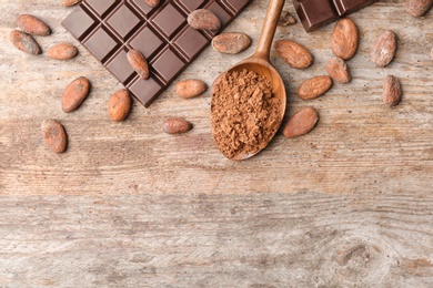 Flat lay composition with cocoa powder, beans and chocolate bar on wooden background