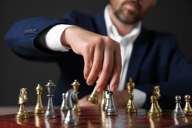 Photo of Man with game pieces playing chess at checkerboard against dark background, closeup