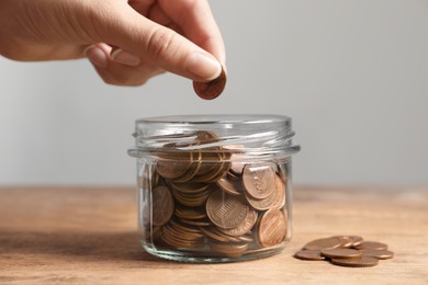 Photo of Woman putting coin in glass jar with money at wooden table, closeup