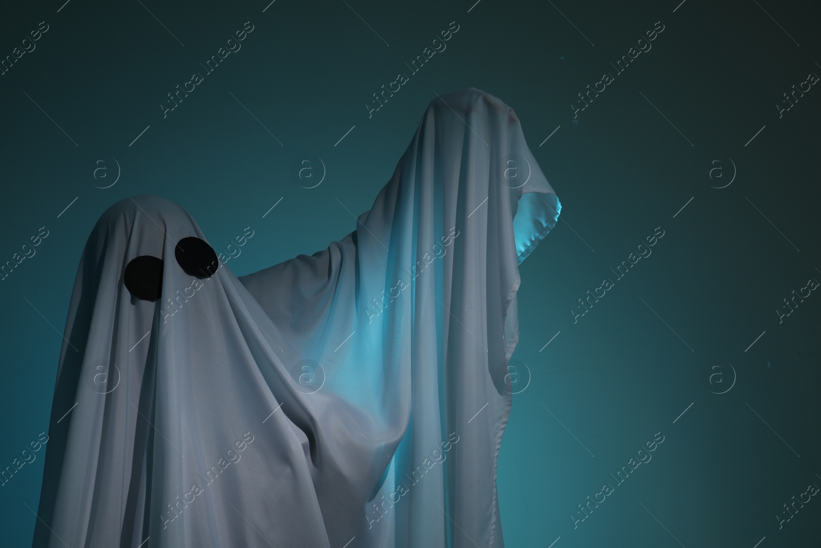 Photo of Creepy ghost. Woman covered with sheet on dark teal background