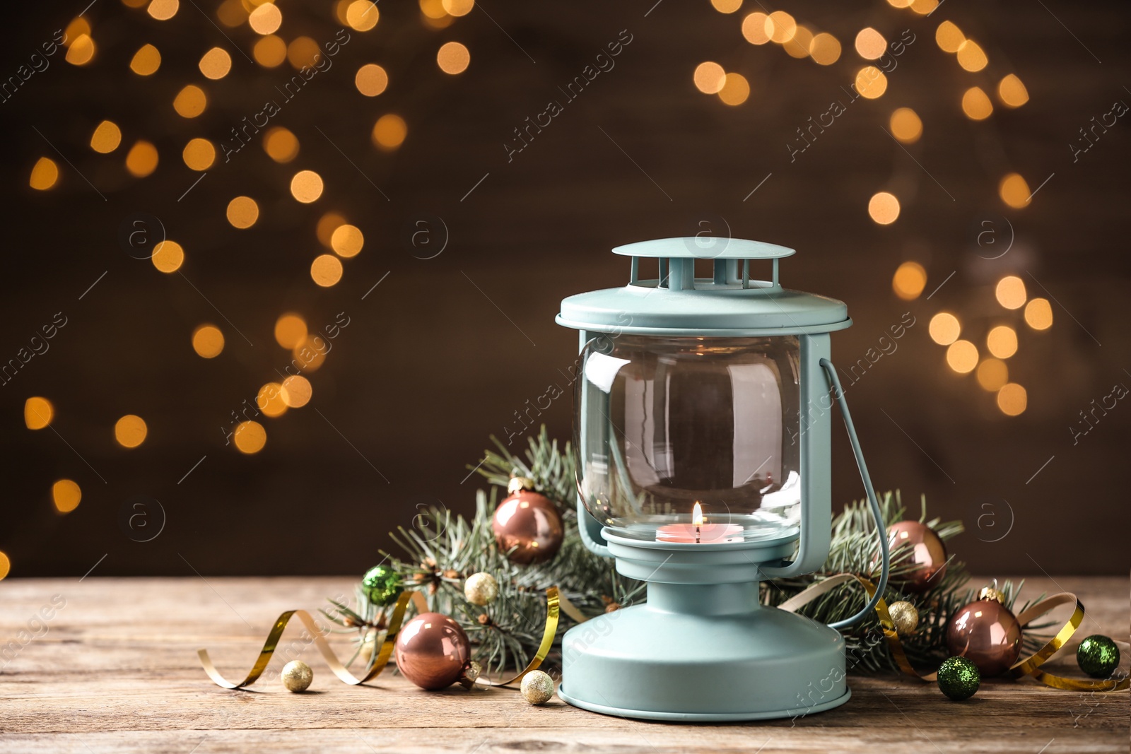 Photo of Lantern and Christmas decor on wooden table against blurred festive lights, space for text. Winter holiday