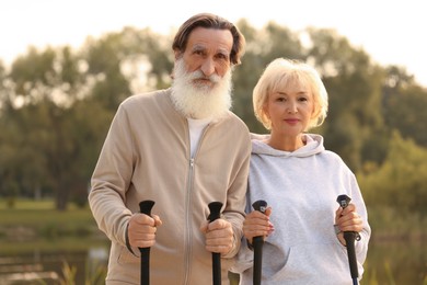 Photo of Senior man and woman with Nordic walking poles outdoors