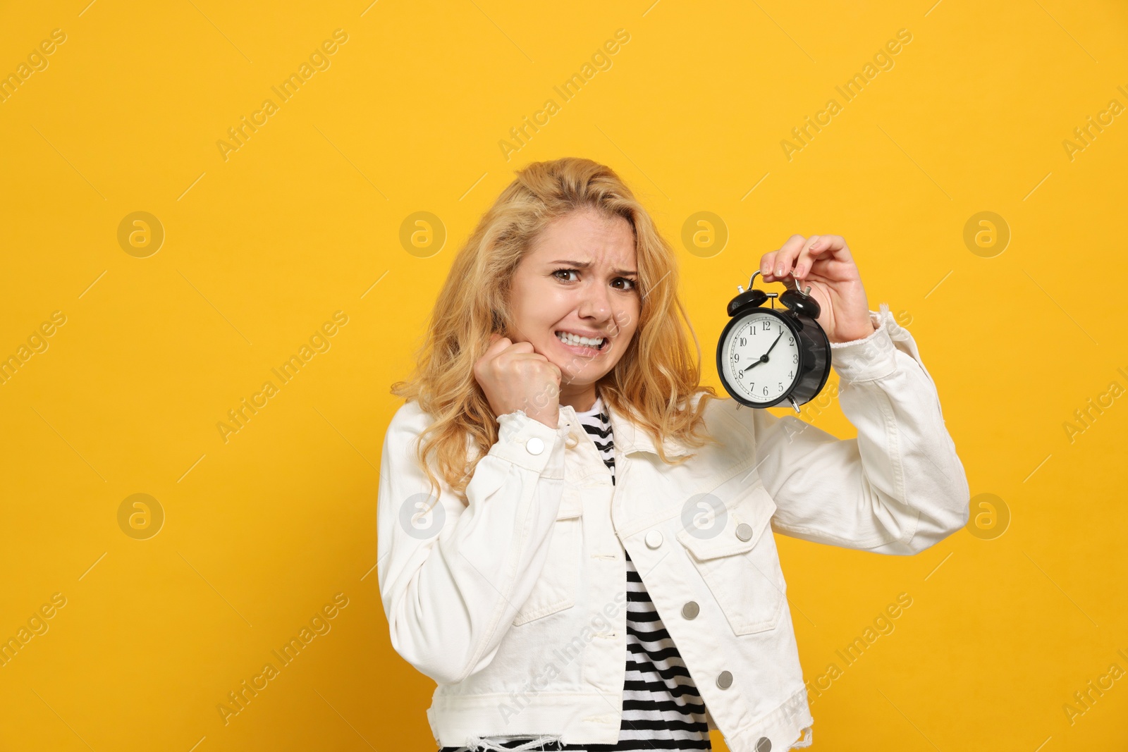 Photo of Emotional woman with alarm clock in turmoil over being late on yellow background