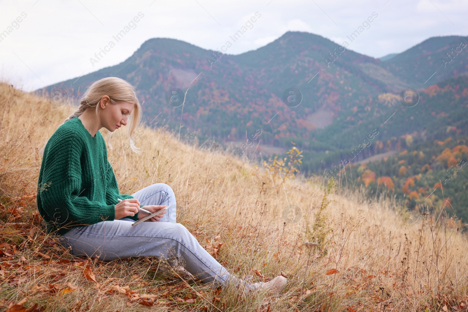 Photo of Young woman drawing on tablet in mountains, space for text