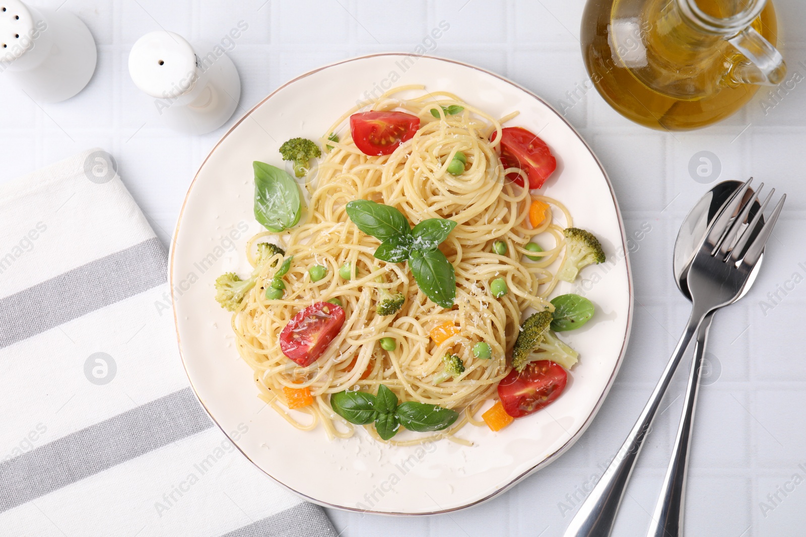 Photo of Delicious pasta primavera with tomatoes, basil and broccoli served on white tiled table, flat lay